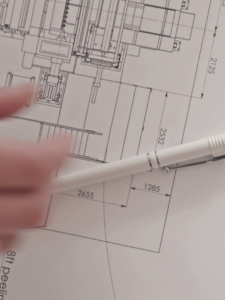Blue print of mechanism with pen and hand hovering over it